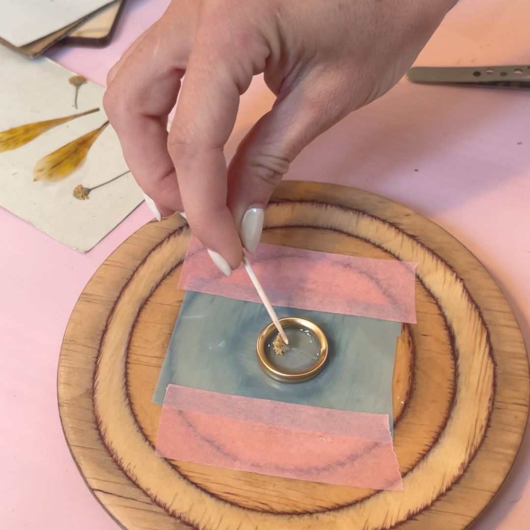 Manos colocando una flor seca en un colgante dorado con resina durante el taller de joyería botánica en Barcelona